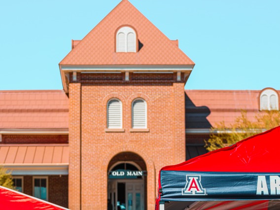Old Main with a tent in front of it that has the UofA logo on the corner